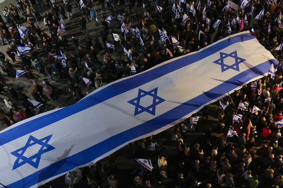 Israelis march with large national flag during a protest against plans by Prime Minister Benjamin Netanyahu's new government to overhaul the judicial system, in Tel Aviv, Israel, Saturday, Feb. 18, 2023. (AP Photo/Tsafrir Abayov)