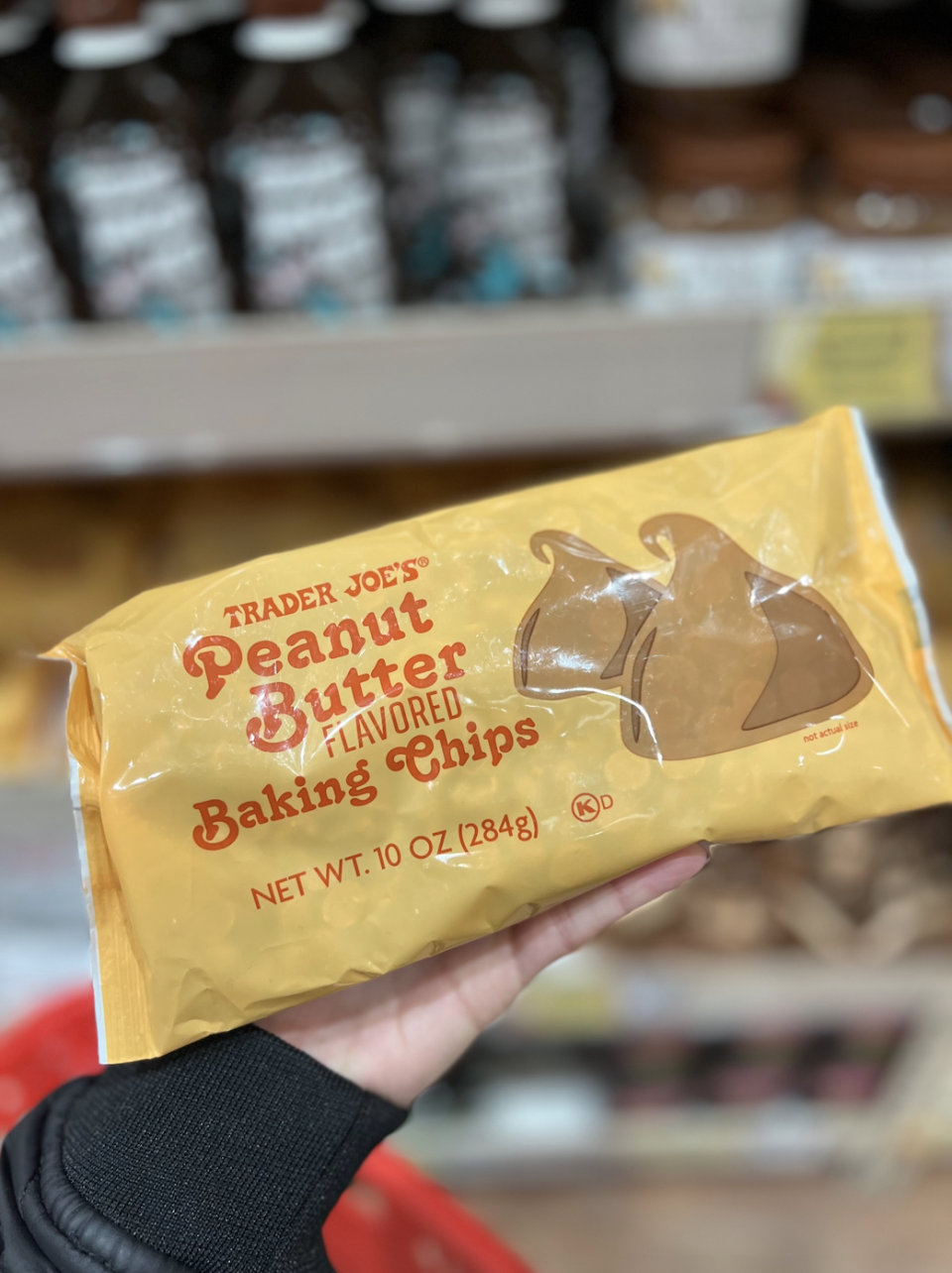 Hand holding a package of Trader Joe's Peanut Butter Baking Chips in a grocery store aisle