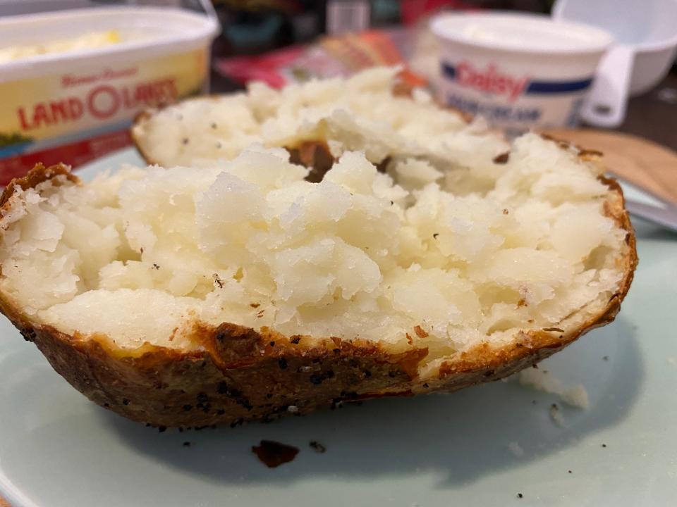 A baked potato sliced open on a plate after being cooked in an air fryer, with tubs of sour cream and butter behind it