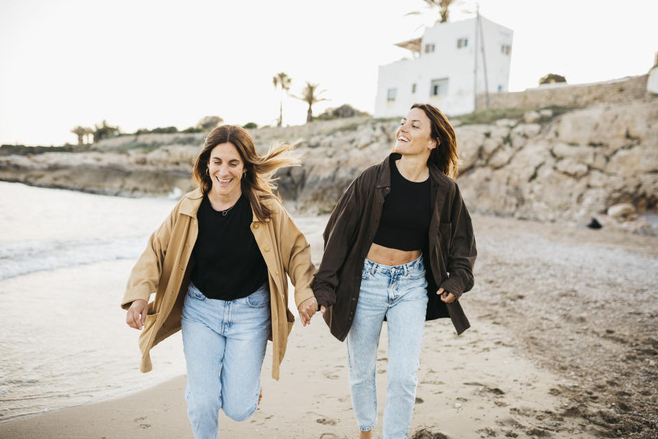 Happy female couple running on the water's edge at the beach