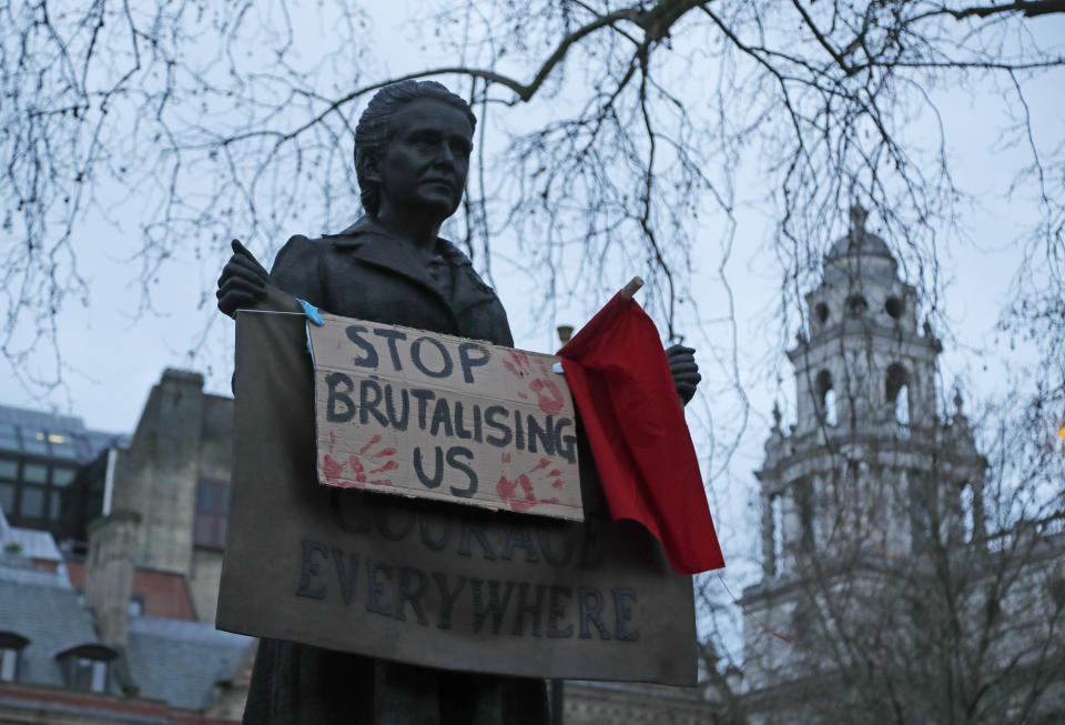 A placard hangs from a statue of suffragist Millicent Garrett Fawcett as demonstrators gather during a protest in Parliament Square in London, Sunday, March 14, 2021. London's Metropolitan Police force was under heavy pressure Sunday to explain its actions during a vigil for Sarah Everard whom one of the force's own officers is accused of murdering. (AP Photo/Frank Augstein)