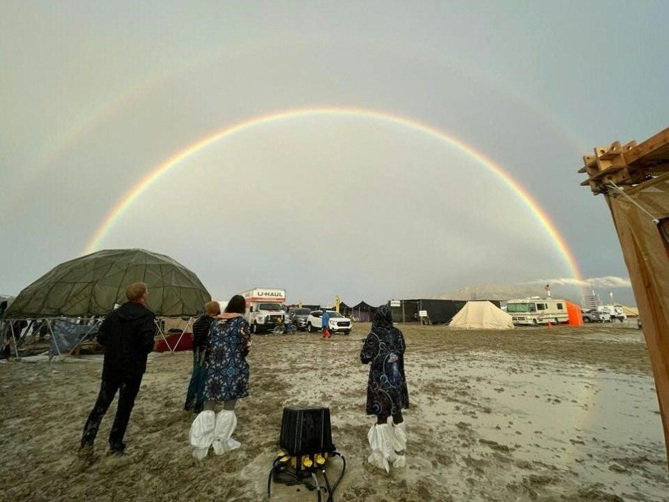 People stand in mud with a double rainbow above them.