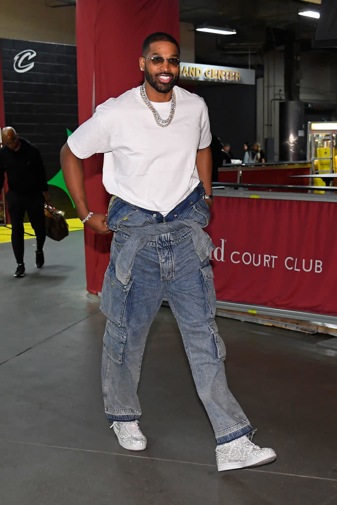 Tristan Thompson is wearing a white t-shirt, baggy blue jeans with multiple pockets, a chain necklace, and silver shoes