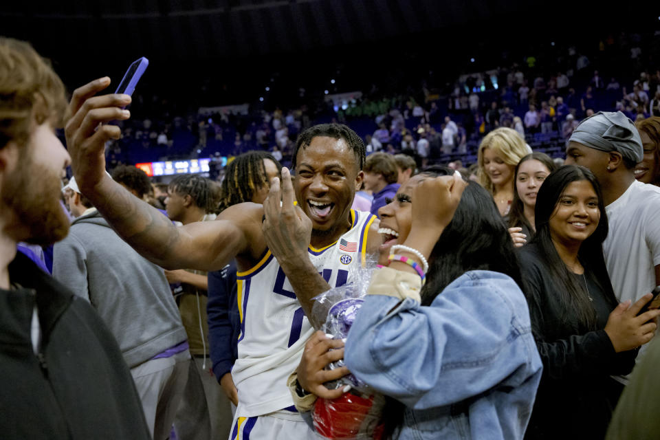 LSU guard Trae Hannibal takes a photo with one of fans who rushed the court after LSU's victory over Kentucky in an NCAA college basketball game in Baton Rouge, La., Wednesday, Feb. 21, 2024. (AP Photo/Matthew Hinton)