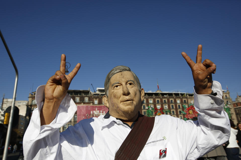 A man wearing a mask depicting Mexico's new President Andres Manuel Lopez Obrador flashes "vee for victory" hand signs as he arrives at the Zocalo where celebrants are gathering for the presidential inaugural festivities, in Mexico City, Saturday, Dec. 1, 2018. Mexicans are getting more than just a new president Saturday. The inauguration of Lopez Obrador will mark a turning point in one of the world's most radical experiments in opening markets and privatization. (AP Photo/Moises Castillo)