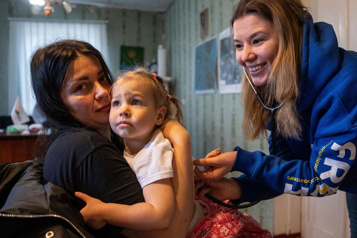 A medical volunteer of Frida Ukraine listens through a stethoscope to the lungs of a girl while providing specialist medical care for civilians in Khrestysche village, Donetsk (AP)