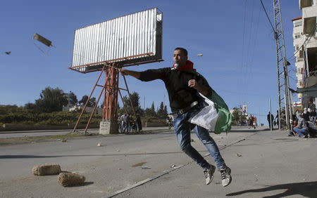 A Palestinian hurls stones at Israeli troops during clashes in the West Bank town of Halhul, north Hebron in this November 14, 2015 file photo. REUTERS/Mussa Qawasma/FIles