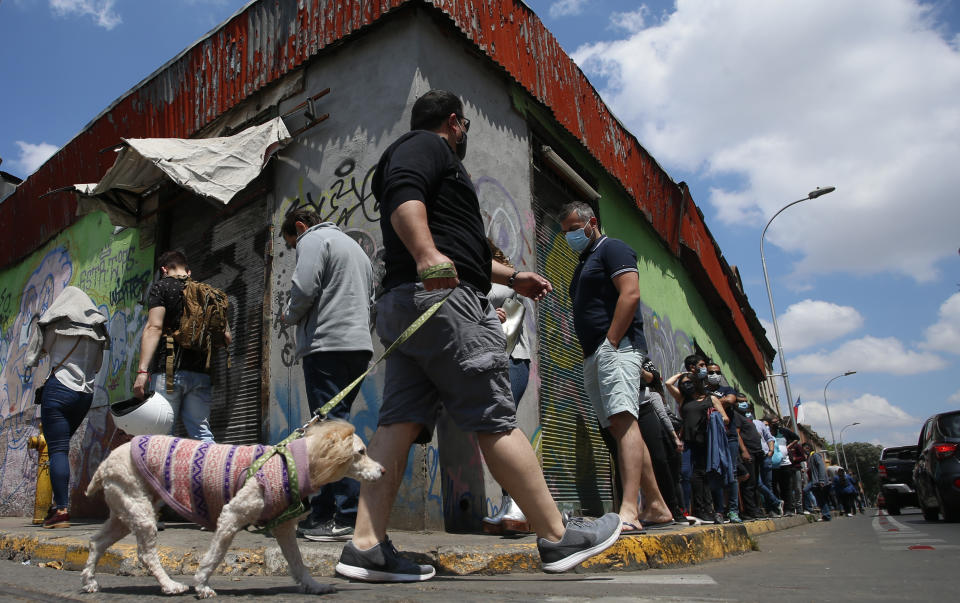 A man walks with his dog past people lining up for their turn to vote during a referendum to decide whether the country should replace its 40-year-old constitution, written during the last dictatorship, in Santiago, Chile, Sunday, Oct. 25, 2020. (AP Photo/Luis Hidalgo)