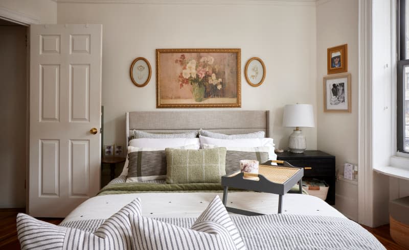 Floral art hangs above bed with striped bedding, throw pillows, and breakfast tray.