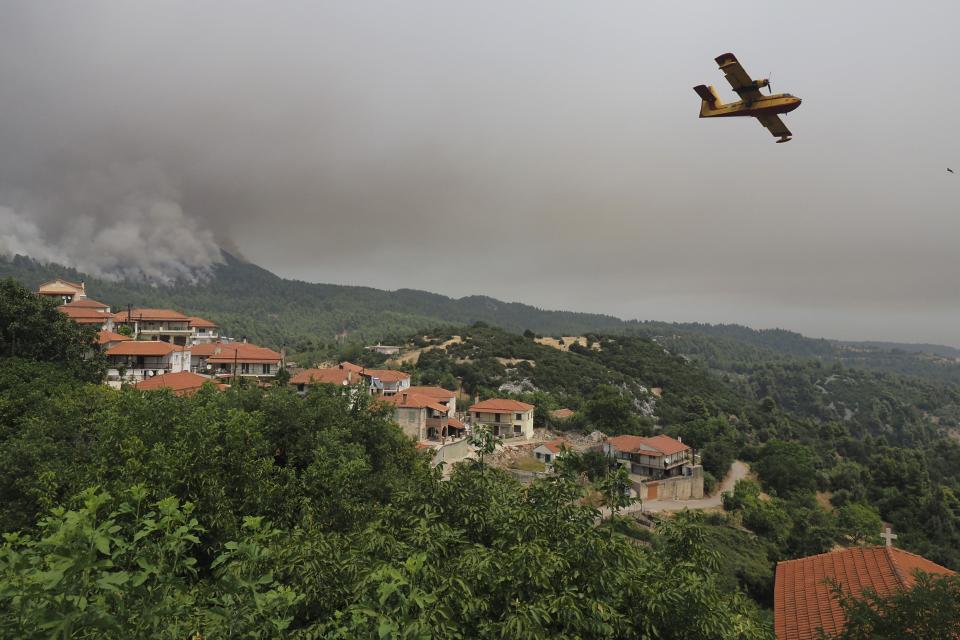 An aircraft operates as flames burn a forest during a wildfire in Kourkouloi village on the island of Evia, about 150 kilometers (93 miles) north of Athens, Greece, Thursday, Aug. 5, 2021. Forest fires fueled by a protracted heat wave raged overnight and into Thursday in Greece, threatening the archaeological site at the birthplace of the modern Olympics and forcing the evacuation of dozens of villages. (AP Photo/Thodoris Nikolaou)