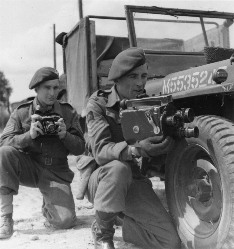 AFPU cameramen Sgt Harry Oakes (left) and Sgt Bill Lawrie kneeling with their stills and movie cameras alongside a jeep. - AFPU/IWM