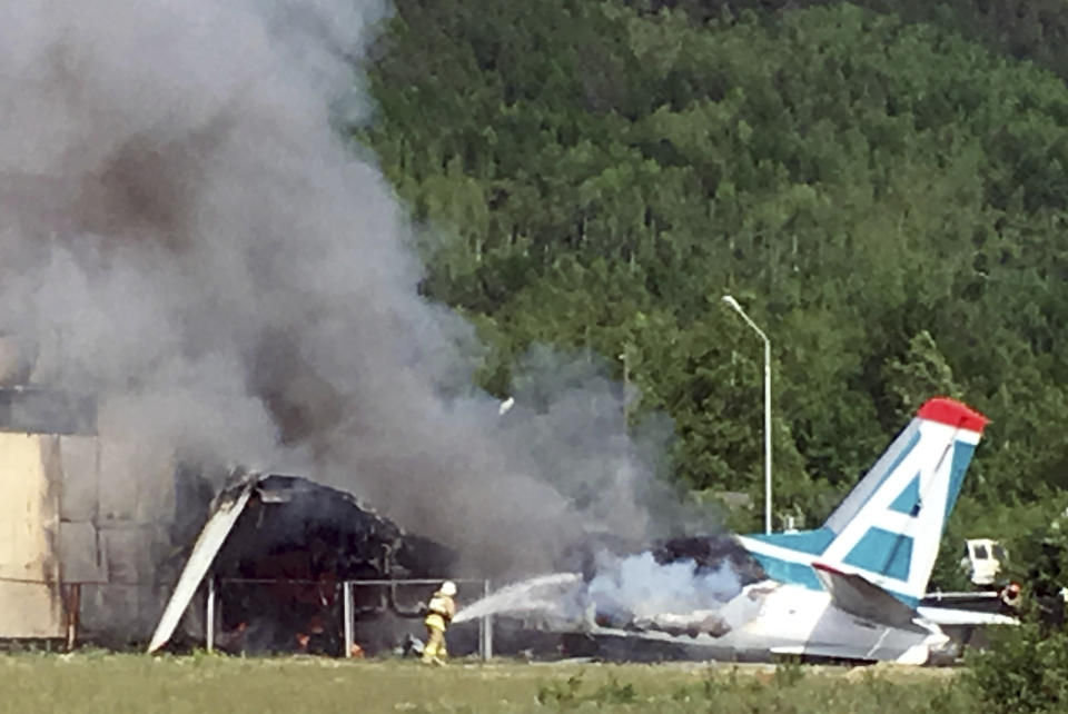 A firemen fights with fire of a plane An-24 after a crash during a landing in Nizhneangarsk, Republic of Buryatia, Russia, Thursday, June 27, 2019. According to the Russian Emergency Ministry, the two dead were members of the cabin crew. Forty-six passengers have been rescued, the ministry said. (AP Photo/Vladimir Dozmorov)