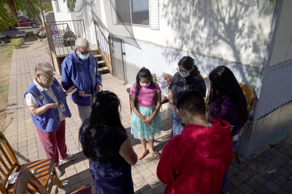 From left, St. Vincent de Paul volunteers Mary Ann Kneip and her husband, Pete Kneip, pray with Zeret Leocadio, 10; her sister, Areli, 9; her brother, Eliel, 12; her mother, Abigail, and her sister Samai, 15, after the Kneips made a delivery from the Emmaus House food pantry Saturday, Nov. 14, 2020, in Phoenix. When her husband, a restaurant cook, was laid off earlier in the pandemic, her income _ barely more than the $11 state minimum wage _ wasn’t enough to cover their expenses. (AP Photo/Ross D. Franklin)
