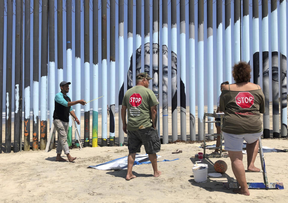 Muralist Mauro Carrera, far left, directs painters working on a new mural on the Mexican side of a border wall in Tijuana, Mexico, Friday, Aug. 9, 2019. The mural shows faces of people deported from the U.S. with barcodes that activate first-person narratives on visitors' phones. Lizbeth De La Cruz Santana conceived the interactive mural in Tijuana as part of doctoral dissertation at the University of California, Davis. (AP Photo/Elliot Spagat)