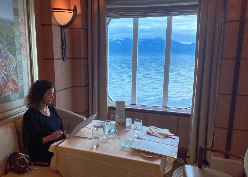 A woman sitting at a table with an ocean view looking at a menu,