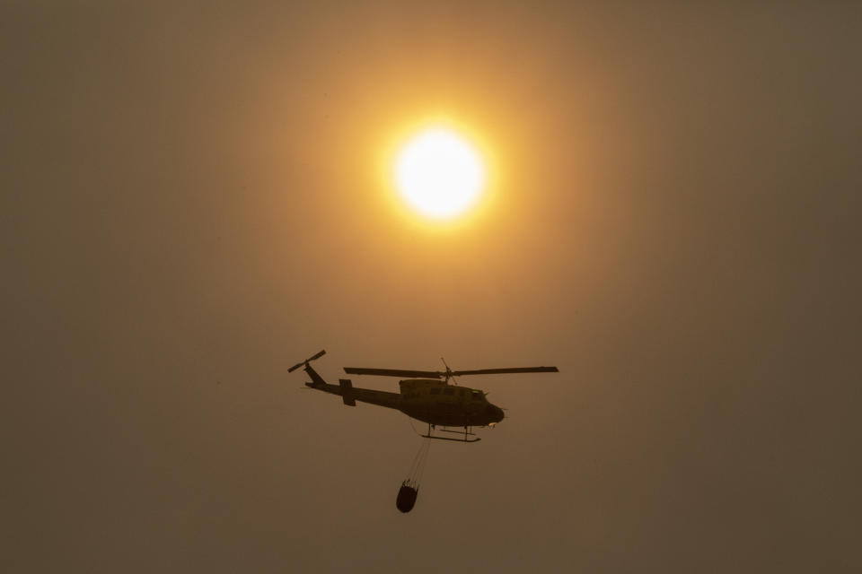 A helicopter flies over a wildfire in Estepona, Spain, Thursday, Sept. 9, 2021. Nearly 800 people have been evacuated from their homes and road traffic has been disrupted as firefighting teams and planes fight a wildfire in southwestern Spain. (AP Photo/Sergio Rodrigo)