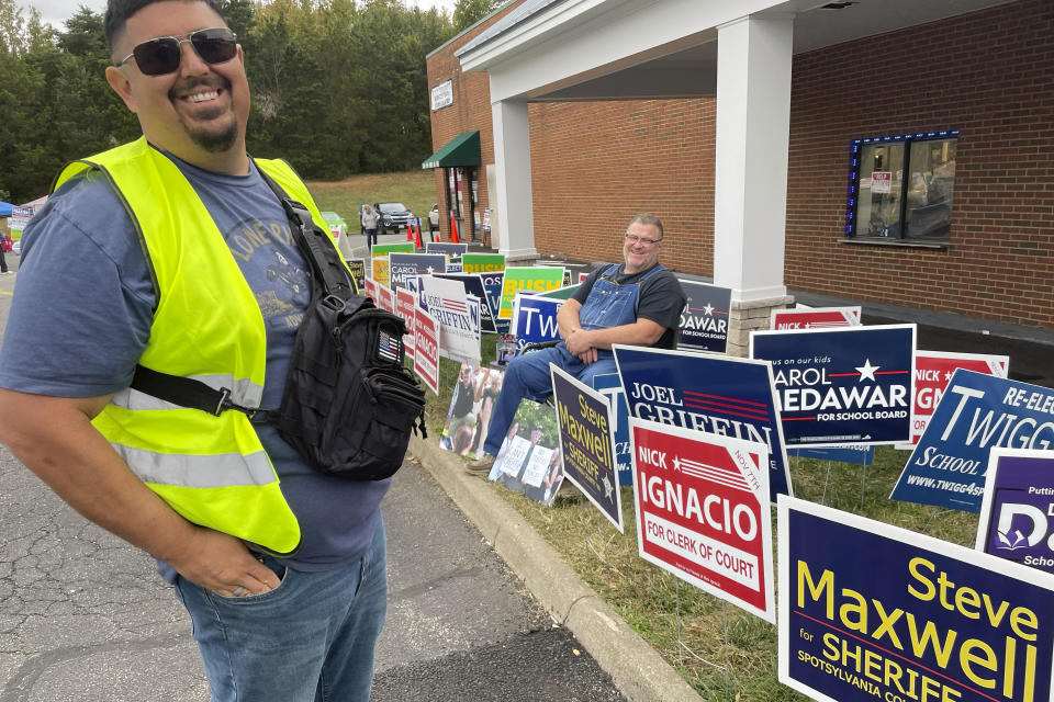 Nick Ignacio, independent candidate for Spotsylvania County clerk of court, stands by a rash of campaign signs at an early voting location in Fredericksburg, Va., on Oct. 17, 2023. Ignacio was handing out misleading sample ballots that implied both parties were endorsing him, though neither is. Republicans and Democrats alike said civility is in short supply in local races for school board and other offices in Tuesday's elections and dirty tricks are widely seen. A judge subsequently barred Ignacio from giving out the sheets. In Virginia, far-right candidates are looking to take over a number of school boards or expand their slim majorities while the left fights fiercely to gain ground. (AP Photo/Cal Woodward)