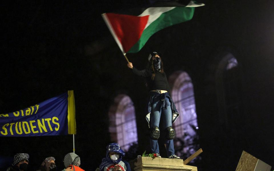 A person inside the encampment waves a Palestinian flag from the barricades