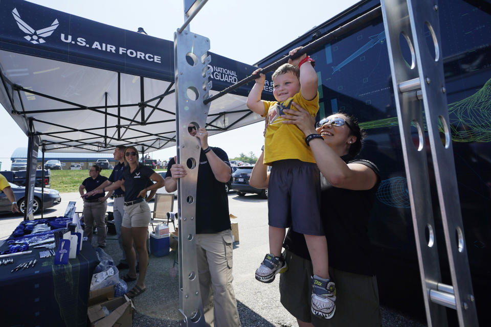 Ryker Morton, 3, is helped while hanging on a chin-up bar while stopping at the U.S. Air Force recruiting tent at the New Hampshire Motor Speedway, Sunday, July 17, 2022, in Loudon, N.H. These are tough times for military recruiters. All services are having problems finding young people who want to join and can meet the physical, mental and moral requirements. Recruiters are offering bigger bonuses and other incentives to those who sign up. And they are seizing on the boost that Hollywood may offer – such as the buzz over Top Gun. (AP Photo/Charles Krupa)