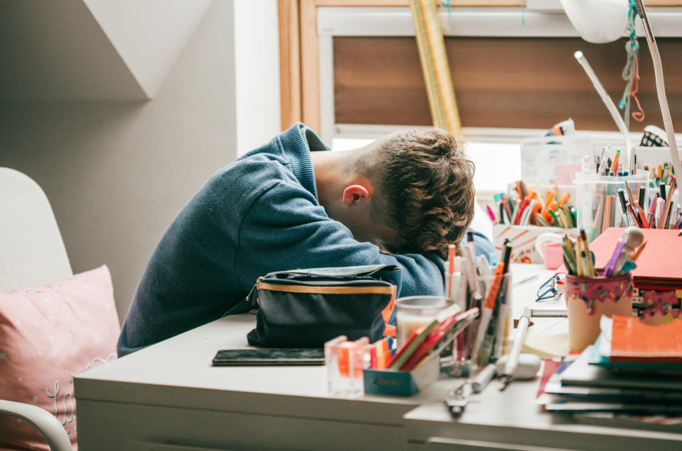 Kid resting head on desk surrounded by art supplies, portraying possible frustration or tiredness while doing creative work