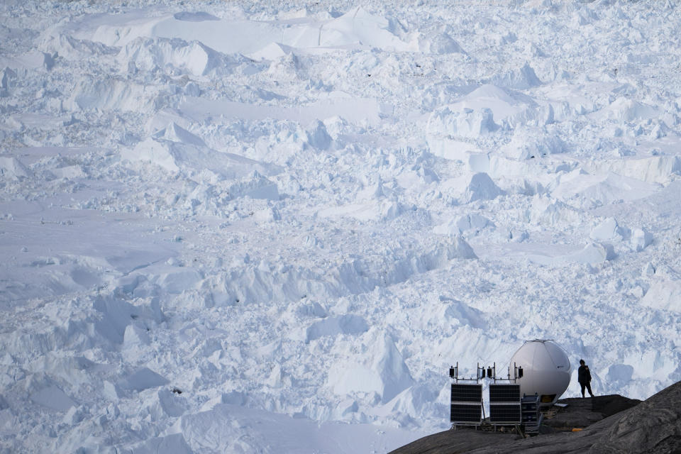 In this Aug. 16, 2019, photo, a woman stands next to an antenna at an NYU base camp at the Helheim glacier in Greenland. Summer 2019 is hitting the island hard with record-shattering heat and extreme melt. Scientists estimate that by the end of the summer, about 440 billion tons of ice, maybe more, will have melted or calved off Greenland's giant ice sheet. (AP Photo/Felipe Dana)
