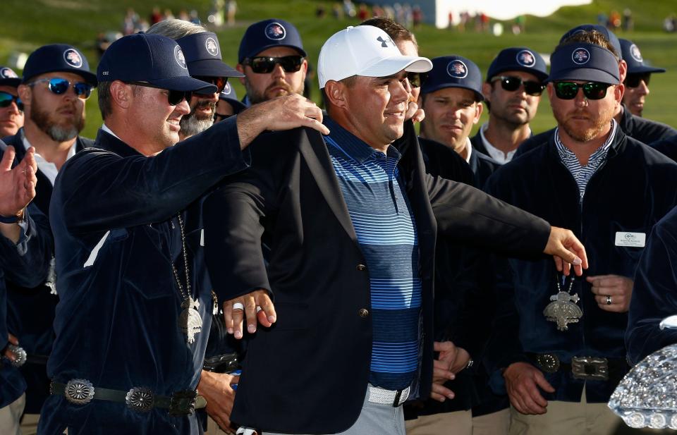 Gary Woodland, al frente a la derecha, recibe ayuda de los Thunderbirds para ponerse la chaqueta azul después de su victoria en los playoffs por un hoyo en la ronda final del torneo de golf Waste Management Phoenix Open el domingo 4 de febrero de 2018 en Scottsdale, Arizona ( Foto AP/Ross D. Franklin)