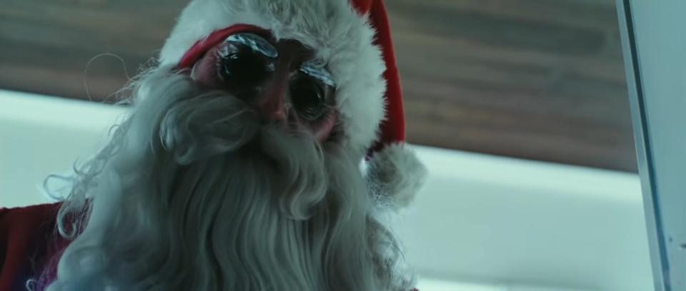 A man in a creepy Santa mask stares through a glass window