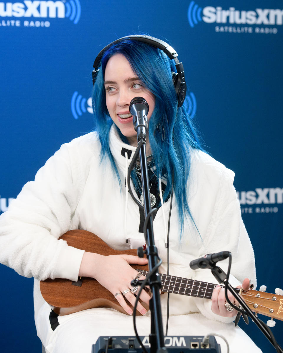 Billie Eilish holding a ukelele as she performs with headphones on
