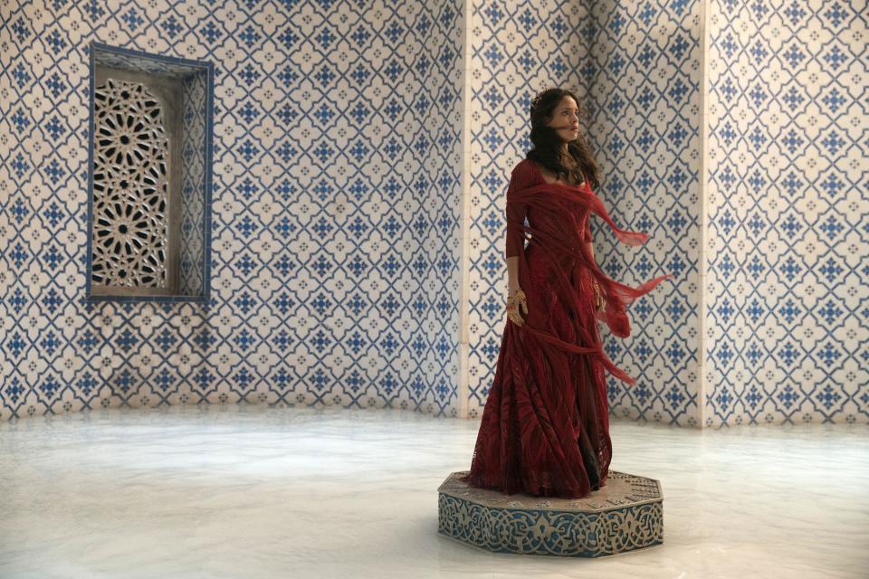 A woman in a flowing red dress stands inside an ornate white-and-blue room