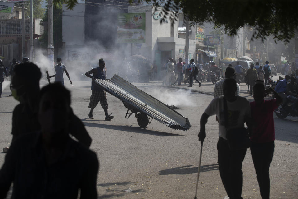 A man pushes a wheelbarrow past a burning barricade set up by friends and relatives of James Philistin who was kidnapped last night, in Port-au-Prince, Haiti, Wednesday, Nov. 24, 2021. (AP Photo/Odelyn Joseph)