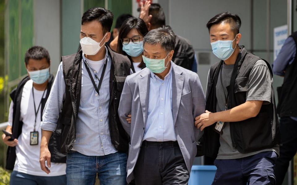 Apple Daily COO Royston Chow Tat Kuen (C) is escorted by police officers as he leaves the office - Shutterstock