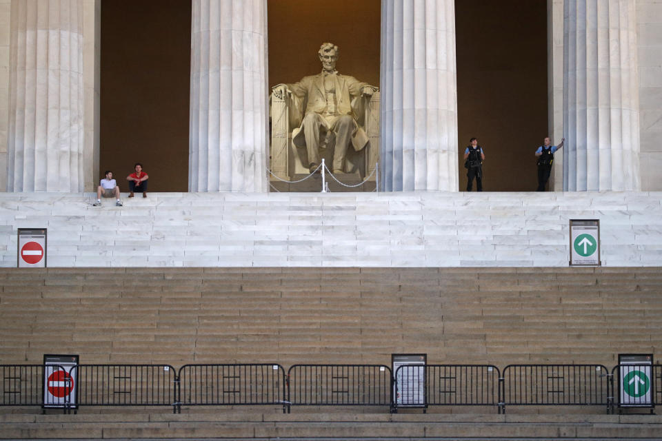 FILE - This Sunday, June 7, 2020 file photo shows visitors, left, and members of the U.S. Park Police, right, at the Lincoln Memorial as sunrise nears in Washington, the morning after massive protests over the death of George Floyd, who died after being restrained by Minneapolis police officers. On Friday, June 12, 2020, The Associated Press reported on a manipulated photo circulating online depicting the statue of Abraham Lincoln covered in graffiti and “BLACK + BROWN LIVES MATTER” written on the wall. The Lincoln statue and surrounding monument were not vandalized during recent protests, according to a spokesman for the National Mall and Memorial Parks, although some graffiti was left at the steps leading up to the monument. (AP Photo/Patrick Semansky)