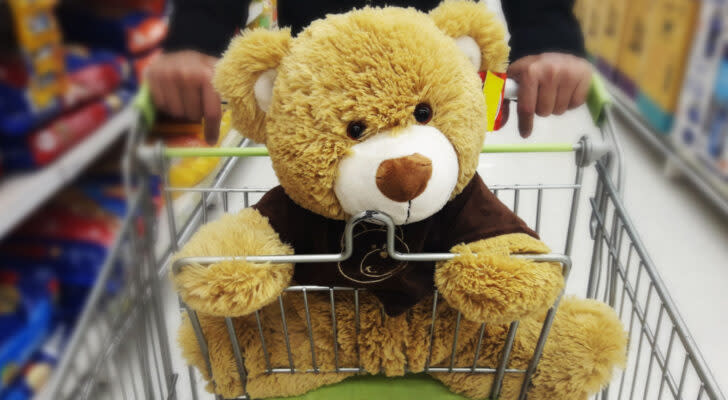 A stuffed teddy bear wearing a brown shirt in a grocery store shopping cart.