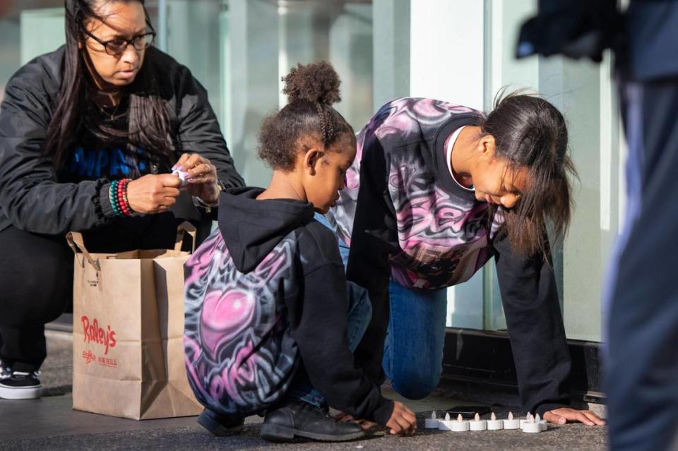 The daughters of Sergio Harris arrange candles to form his initials before a press conference on Monday, April 3, 2023, to mark the one-year anniversary of the mass shooting in downtown Sacramento. Sergio Harris was one of six who was shot and killed on April 3, 2022. Leia Schenk, left, founder of social justice community organization Empact, watches at left.