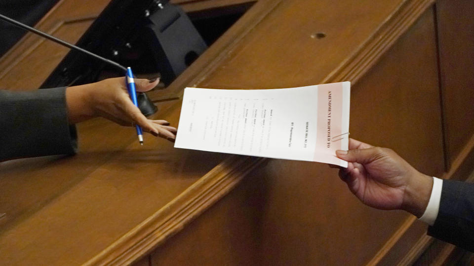 An amendment to legislation that would limit how race can be taught in schools and universities is passed by a lawmaker, right, to an assistant clerk of the House in the Chamber to be read, Thursday, March 3, 2022, at the Mississippi Capitol in Jackson. The amendment was defeated. (AP Photo/Rogelio V. Solis)