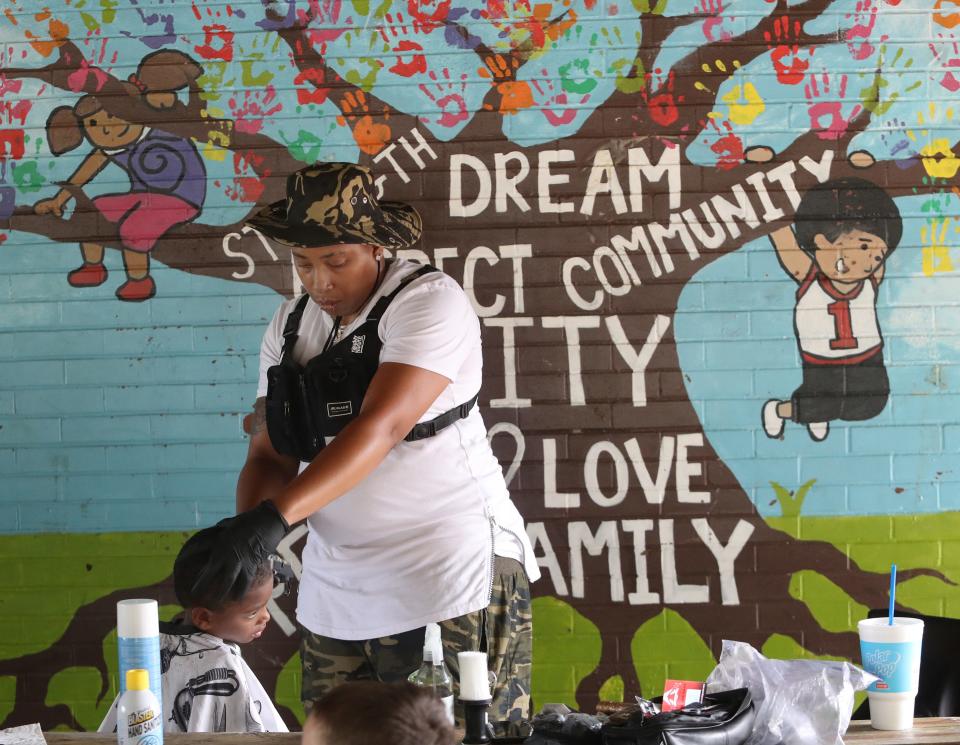 Patrick Benson, 6, lower left, sits patiently as Biance Hooten of One Chop Shop in Canton cuts his hair in front of the pavilion mural at the annual Back to School and Community Day at Thompson Snodgrass Park on Saturday, Aug. 12, 2023.