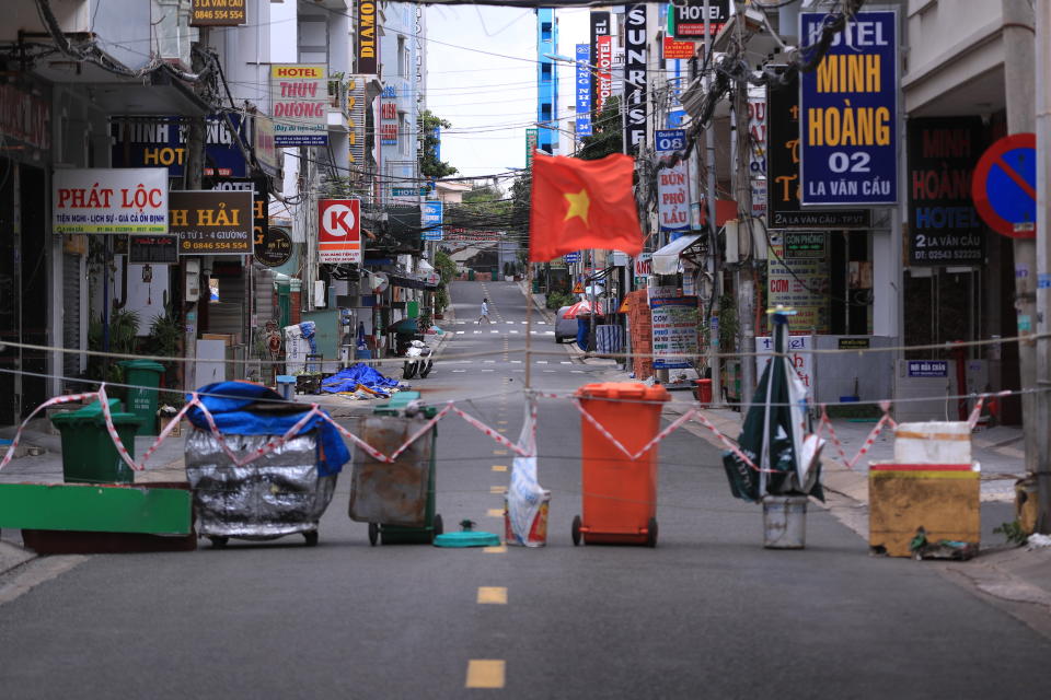 An alley is blocked with trash can and a Vietnamese flags in Vung Tau, Vietnam, Monday, Sept. 13, 2021. In Vung Tau, just outside Ho Chi Minh city, streets are sealed and checkpoints are set up to control the movement of people. Barbed wire, door panels, steel sheets, chairs and tables are among materials being used to fence up alleys and isolate neighborhoods.(AP Photo/Hau Dinh)