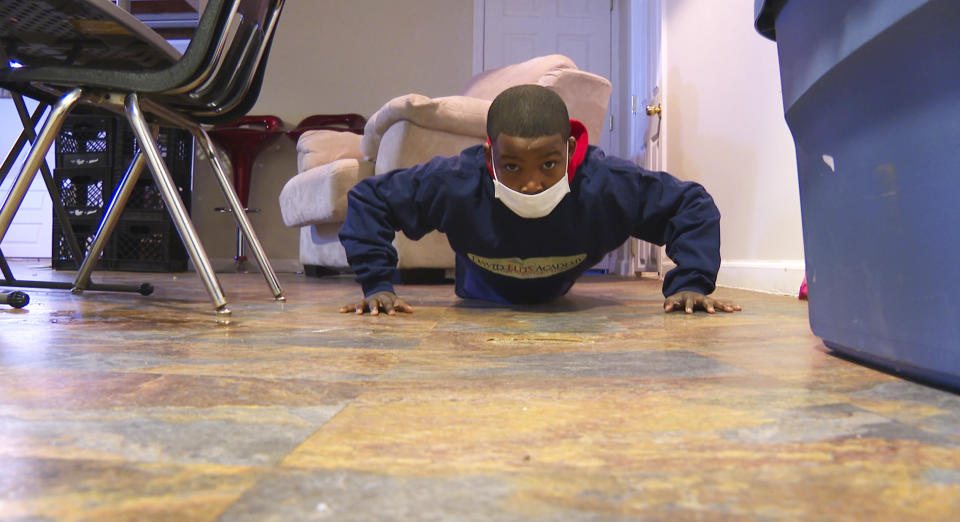 In this image made from video, Deion Hollis does push-ups during his fifth-grade physical education class at a home in Oak Park, Mich., Tuesday, Feb. 9, 2021. Deion and most of his classmates at David Ellis Academy take P.E. and other classes virtually due to the coronavirus pandemic. (AP Photo/Mike Householder)