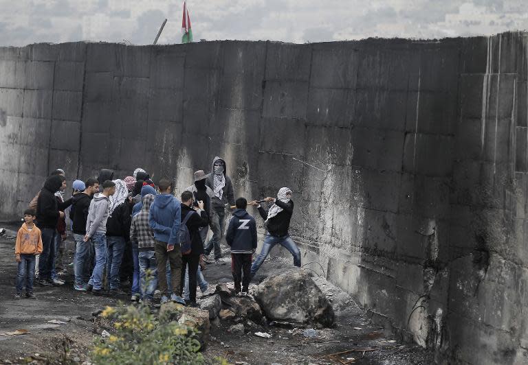 A masked Palestinian youth tries to hammer a hole in Israel's controversial barrier that separates the West Bank town of Abu Dis from Jerusalem during a protest on November 17, 2014