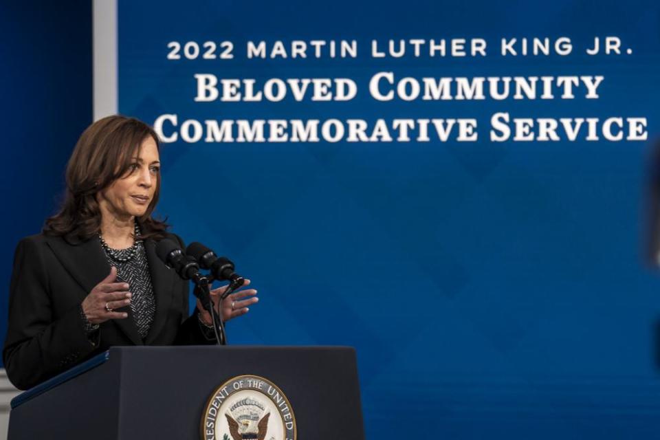 Harris stands at a podium in front of a screen proclaiming 