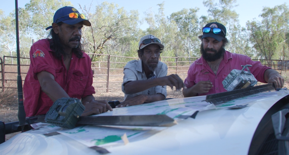 Three Indigenous men look at a map of the Kimberley property on the bonnet of a ute.