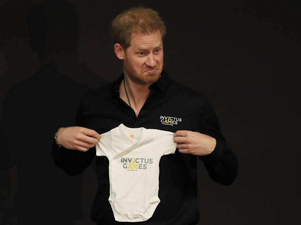 Britain's Prince Harry holds up an outfit for his newborn son, presented by Princess Margriet of the Netherlands, at the launch of the 2020 Invictus Games, in The Hague, Netherlands, Thursday, May 9, 2019. Prince Harry returned to his royal duties Thursday after the birth of his son Archie Harrison, to launch the countdown for the fifth Invictus Games sports competition for injured service personnel and veterans. (AP Photo/Peter Dejong)