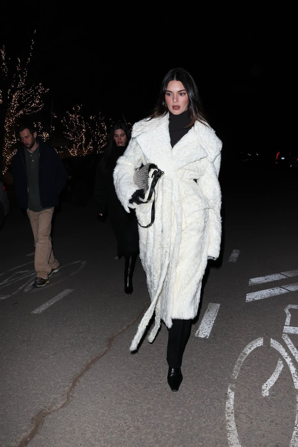 kendall in a white coat walking down a street with people in the background
