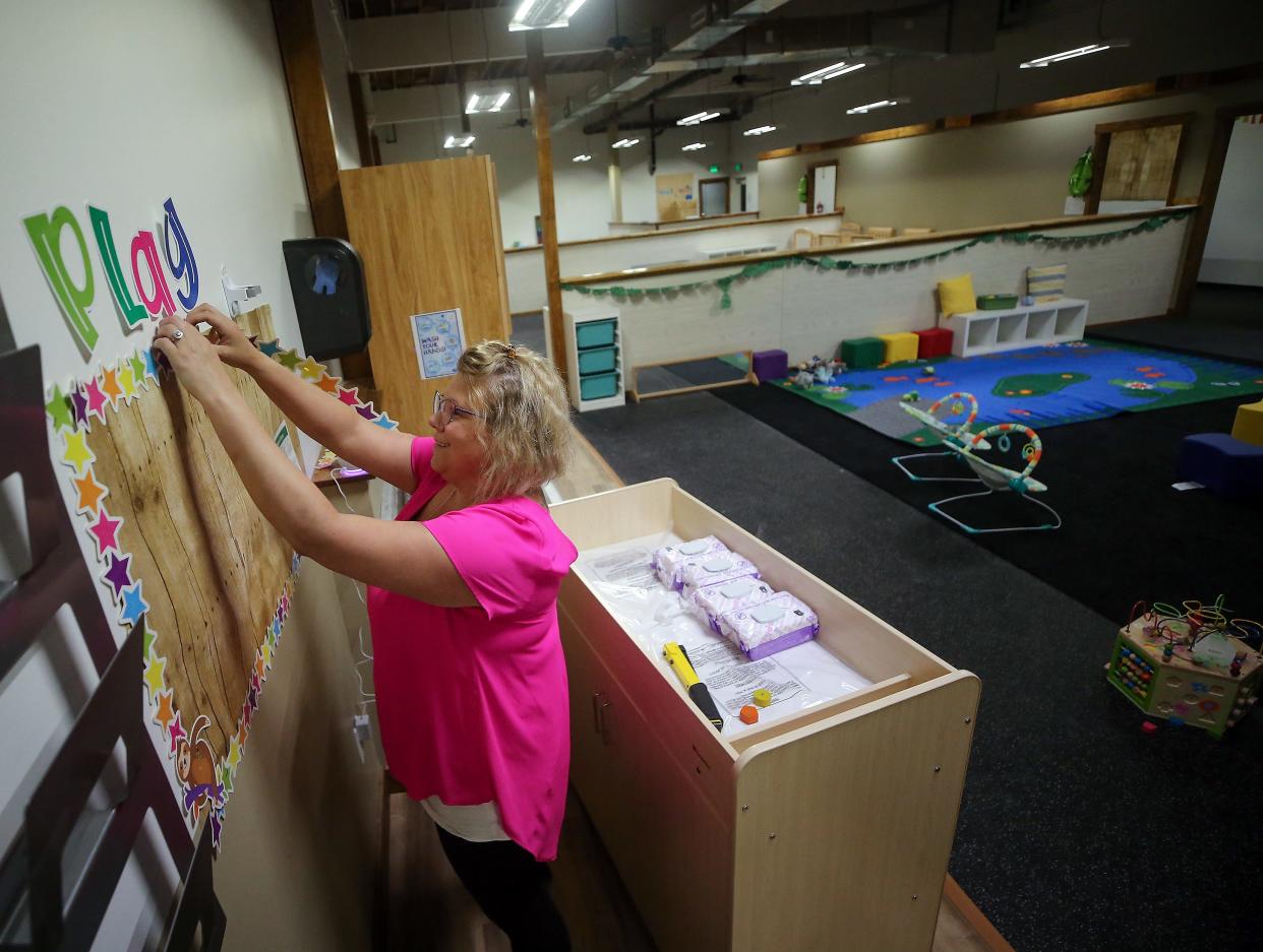 Katie Hudkins hangs a decorative bulletin board as she readies one of the infant areas at her Treetop Village Campus and Infant Center in Port Orchard on Monday, April 29, 2024.