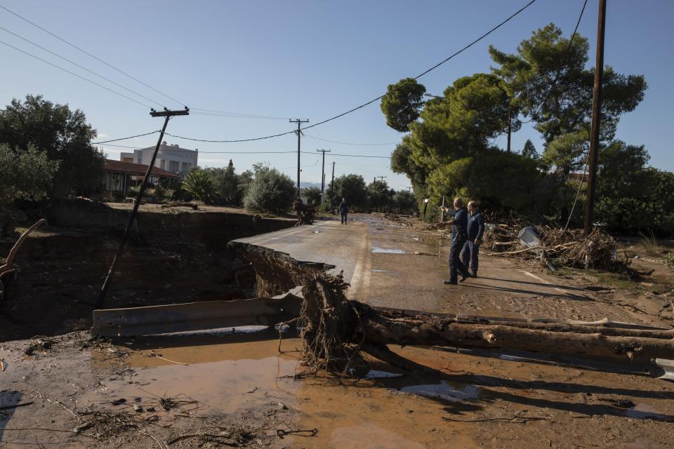 People inspect a damaged road after storms in Kineta village, about 68 kilometers (42 miles) west of Athens, Monday, Nov. 25, 2019. Authorities in Greece say two people have died and hundreds of homes have been flooded following an overnight storm that affected areas west of Athens. (AP Photo/Petros Giannakouris)