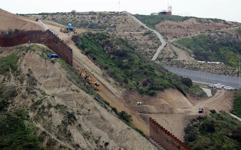 Construction crews replace a section of the primary wall separating San Diego, above right, and Tijuana, Mexico - Credit: Gregory Bull/AP