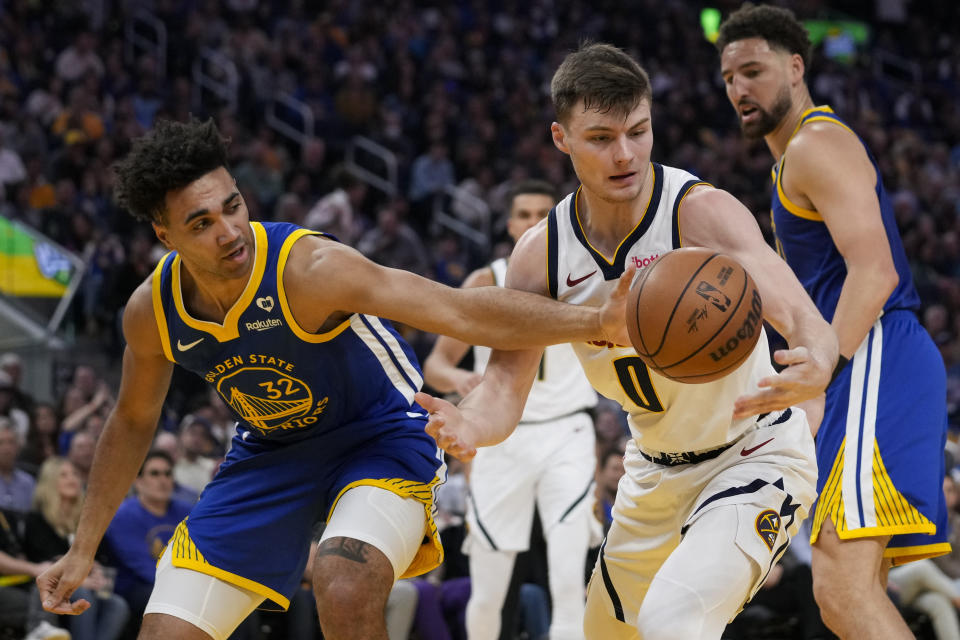 Golden State Warriors forward Trayce Jackson-Davis, left, and Denver Nuggets guard Christian Braun (0) compete for possession of the ball during the first half of an NBA basketball game Sunday, Feb. 25, 2024, in San Francisco. (AP Photo/Godofredo A. Vásquez)