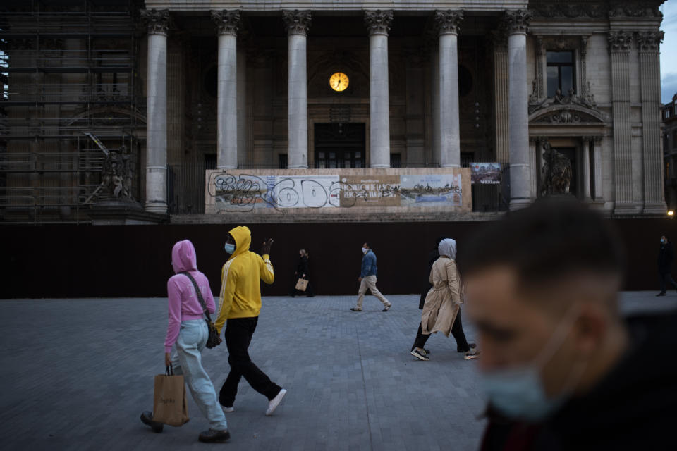 Passers-by, wearing face masks to prevent the spread of the coronavirus, walk past a clock installed at the La Bourse, former stock exchange, building during an autumn evening prior to the curfew in downtown Brussels, Friday, Oct. 23, 2020. (AP Photo/Francisco Seco)