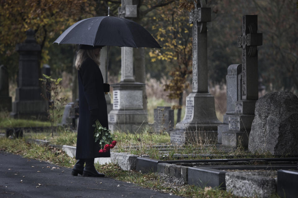 woman with an umbrella standing at a grave