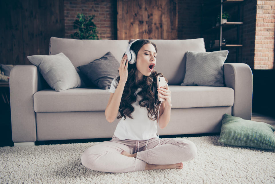 Girl sitting on the floor in front of a couch while wearing headphones and singing into her phone